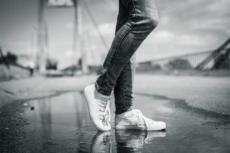 Foots of a woman in a sport shoes flying over a puddle diring jumping. Close up shot of foots over...