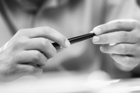 Man's hands holding a black pen in both arms in a thinking gesture during a meeting or negotiation.  Black and white imageの写真素材