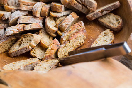 Slices of brown bread in a wooden bowl with iron tongsの写真素材