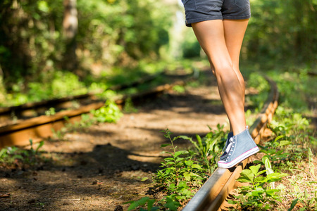 Young woman with beautiful sporty legs walking on rails in jeans sneakers