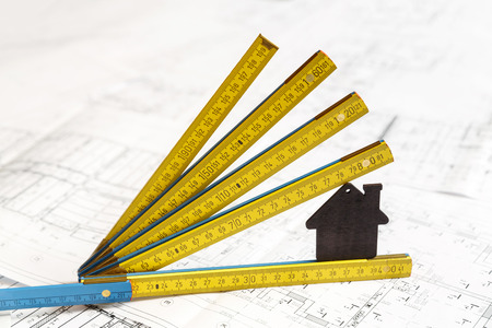 Image of small black toy house and a collapsible yellow and blue ruler standing on top of architecture blueprint planの写真素材