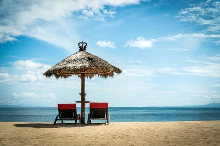 Two red beach chairs under wicker umbrella on a coast. Idyllic holiday landscape conceptの写真素材