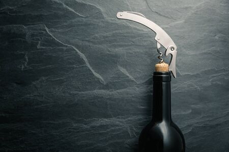 Stainless  wine corkscrew in a cork of wine bottle neck on a black rocky slate background