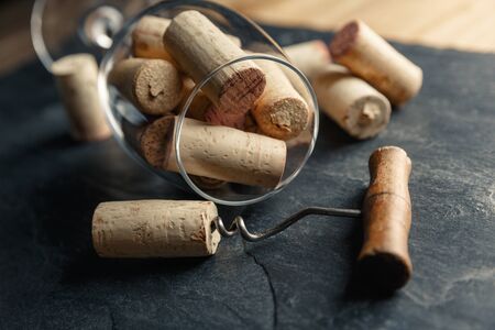 Wine corkscrew with a cork and wine glass full of corks on a black rocky slate backgroundの写真素材