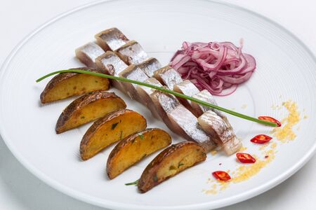 Herring fillet slices with roasted potatoes on a white plate.  Restaurant servingの写真素材