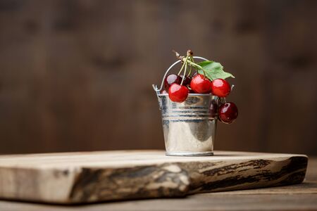 Sweet cherry in small decorative metal bucket on a wooden board on a brown wooden backgroundの写真素材
