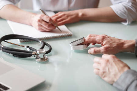 Doctor measures patient's oxygen saturation and pulse using pulse oximeter in a clinic. Health care conceptの写真素材