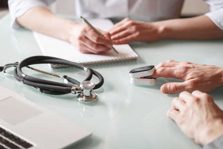 Doctor measures patient's oxygen saturation and pulse using pulse oximeter in a clinic. Health care conceptの写真素材