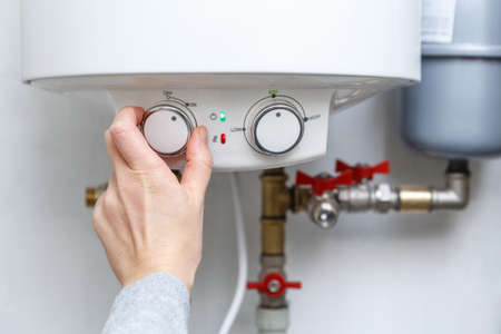 Female hand turning on electric water heater (boiler). Household enegry saving equipmentの写真素材
