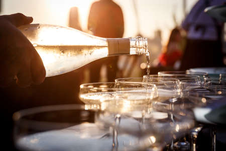 Sunset closeup view of a Waiter's hand pouring sparkling wine into glasses at a party. Hospitality and catering service conceptの写真素材