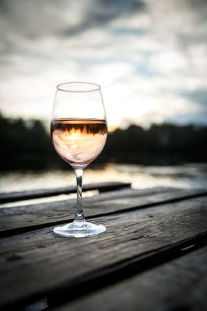 Sunset view of a glass of orange wine on a wooden pier on a lake. Wine drinking on a beautiful locationの写真素材
