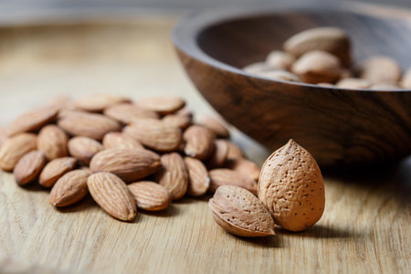 Peeled raw almonds and almonds in a shell in a wooden bowl on a wooden background. Nuts, nutrition and raw food conceptの写真素材