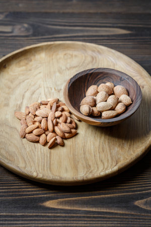 Peeled raw almonds on a wooden plate and almonds in a shell in a wooden bowl on a wooden background. Nuts, nutrition and raw food conceptの写真素材