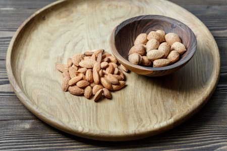 Peeled raw almonds on a wooden plate and almonds in a shell in a wooden bowl on a wooden background. Nuts, nutrition and raw food conceptの写真素材