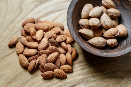 Peeled raw almonds and almonds in a shell in a wooden bowl on a wooden background. Nuts, nutrition and raw food conceptの写真素材