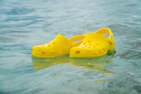 Lightweight pvh syellow slippers swimming on a water surface. Convenient footwear concept