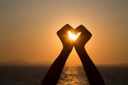 Silhouettes hand heart shaped with sun sets and the sky orangeの写真素材