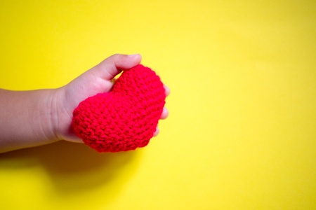 Red heart in child hand on yellow background. Kindness concept, gift, hand made valentine, close up, horizontal, copy spaceの写真素材
