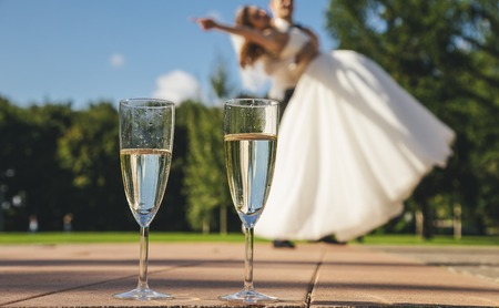 Two glasses with wine on the background of the blurred danced bride and groom.の写真素材