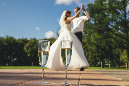 Two glasses with wine on the background of the blurred danced bride and groom.の写真素材