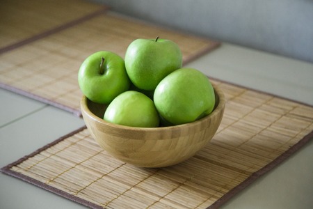 green fresh apples are in a wooden bowl in the kitchenの写真素材