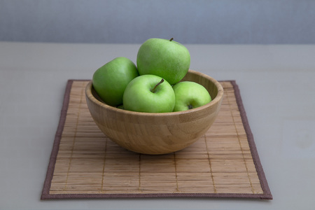 green fresh apples are in a wooden bowl in the kitchenの写真素材
