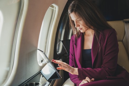 beautiful young woman sits in a plane and works on laptopの写真素材