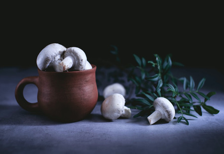 Champignon mushrooms in an old clay pot on a table in a darkの写真素材