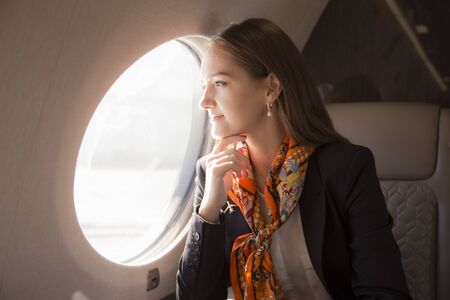 Beautiful young woman sits in a plane near the window and look outside at sunny dayの写真素材