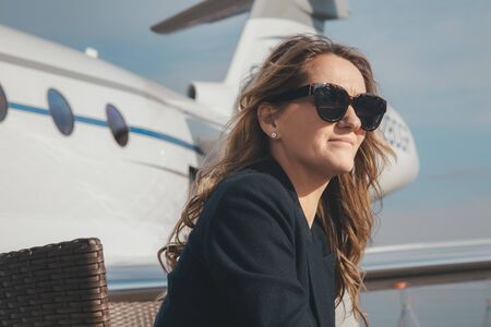 Beautiful businesswoman is seating near the business jet airplane at a sunny dayの写真素材