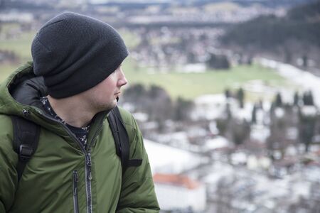 Male tourist in a green jacket with a backpack looks at the mountainsの写真素材