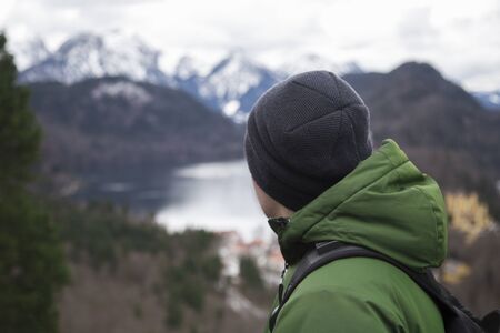 Male tourist in a green jacket with a backpack looks at the mountains