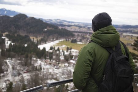 a male tourist in a green jacket with a backpack looks into the distance at the mountainsの写真素材