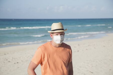 A man with a medical protective mask for coronavirus on the beach in a tropical country at summer sunny dayの写真素材