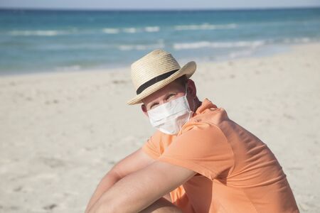 A man with a medical protective mask for coronavirus on the beach in a tropical country at summer sunny dayの写真素材