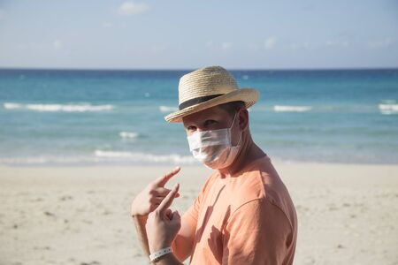 A man with a medical protective mask for coronavirus on the beach in a tropical country at summer sunny dayの写真素材