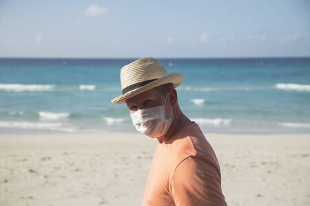 A man with a medical protective mask for coronavirus on the beach in a tropical country at summer sunny dayの写真素材