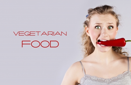 Portrait of a happy, young woman holding red, hot chilli in mouthの写真素材