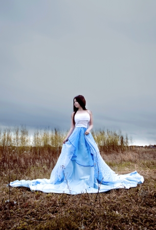 Beautiful young woman with long hair in blue fabric and blue cloudsの写真素材