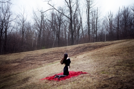 Woman in black dress and long hair sitting on red carpet in cold forestの写真素材
