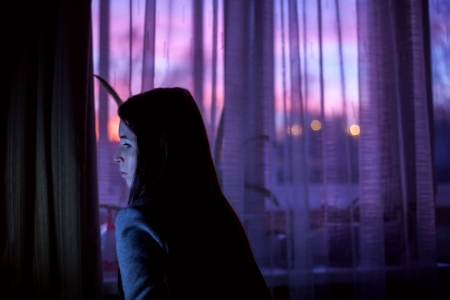 Woman in dark room on sunset window backgroundの写真素材