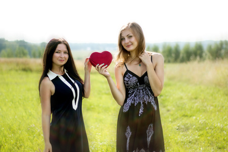 Two pretty women with red heart in sunshine summer fieldの写真素材