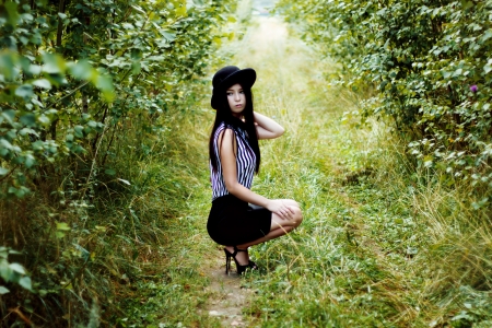 Fashionable woman in black hat sitting in green forestの写真素材