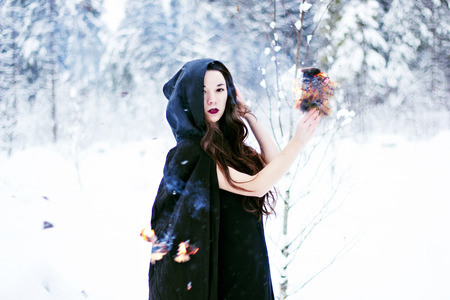 Witch or woman in black cloak with fire ball in white snow forestの写真素材
