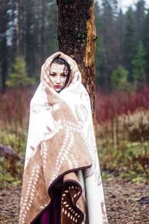 Beautiful woman in warm blanket in forestの写真素材