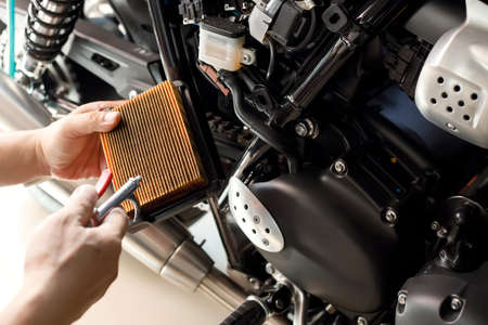 mechanic holding dirty Engine Air Filter over motorcycle and cleaning Filter with air blow gun .mechanic working in garage. Repair service and maintenance motorcycle conceptの写真素材