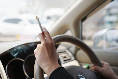 Closeup of woman with finger holding a cigarette and steering wheel while driving car on the motorway . women smoking in carの写真素材