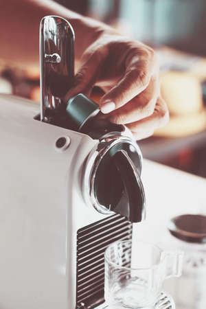 man holding coffee capsules and put in espresso machine with empty cup of coffee at kitchen .