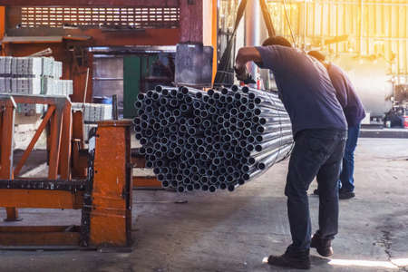 Two workers in uniform using lifting machines to move metal pipe in a sheet metal factory.の写真素材