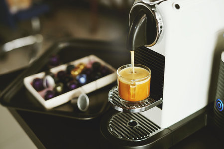 Espresso maker machine breuuing coffee in a glass cup with capsules on white desk at office in the morningの写真素材
